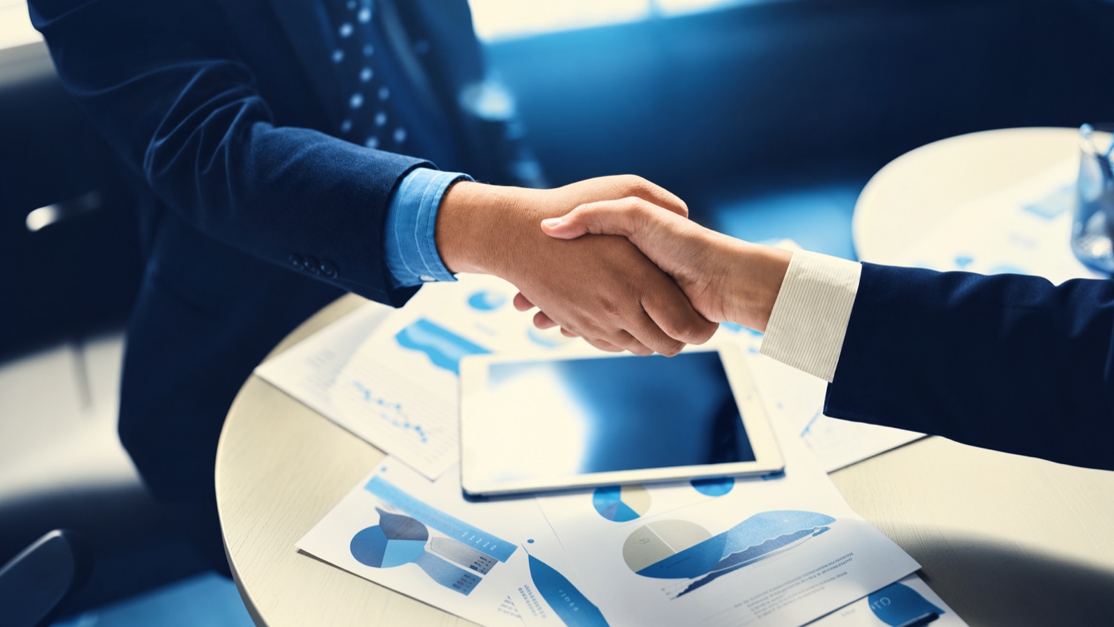 Two people shaking hands over a table of marketing reports
